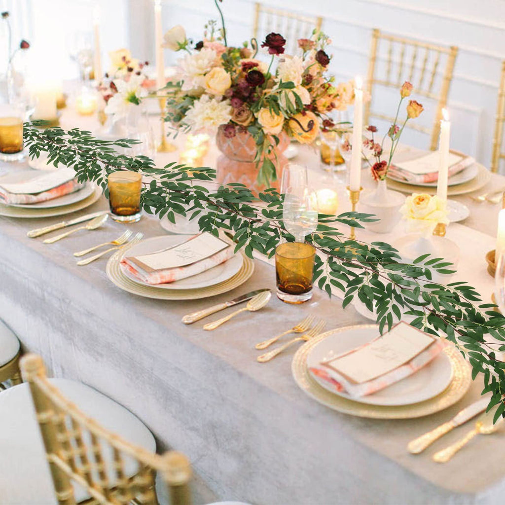 Artificial willow vine garland draped across a formal dining table setting with place settings, candles, and floral arrangements.