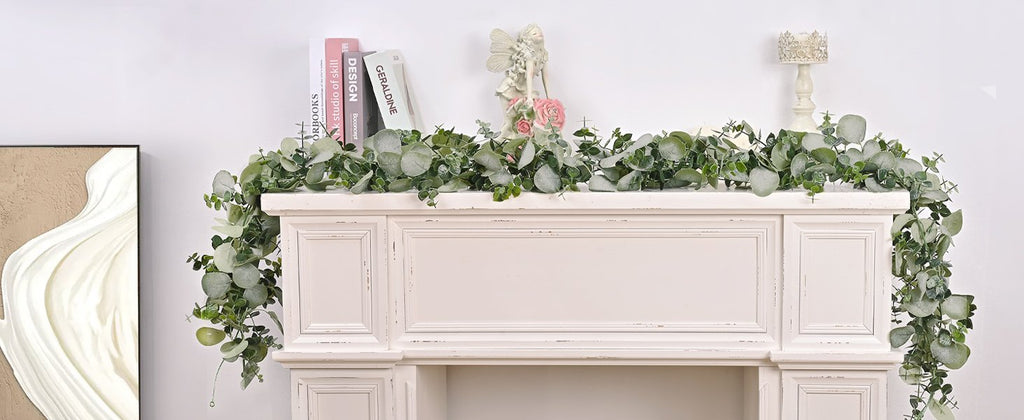 Artificial eucalyptus garland draped over a white mantelpiece with decorative items and books