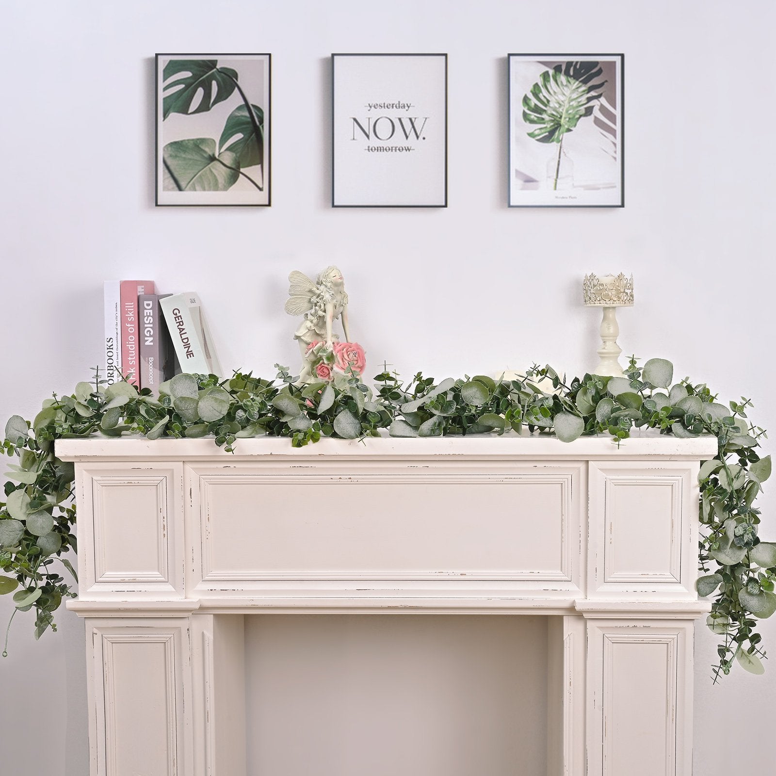 Artificial eucalyptus garland draped over a white mantelpiece with decorative items and framed art above.