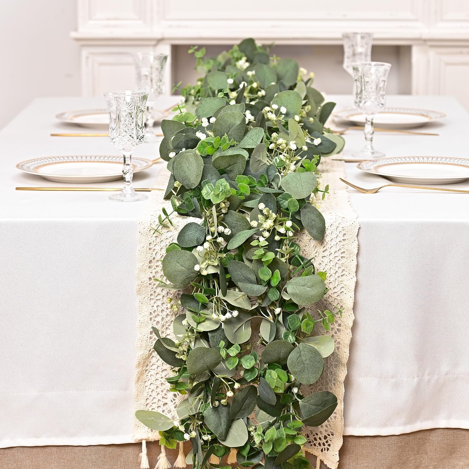 Artificial eucalyptus garland draped across a table runner on a white tablecloth, with place settings visible.