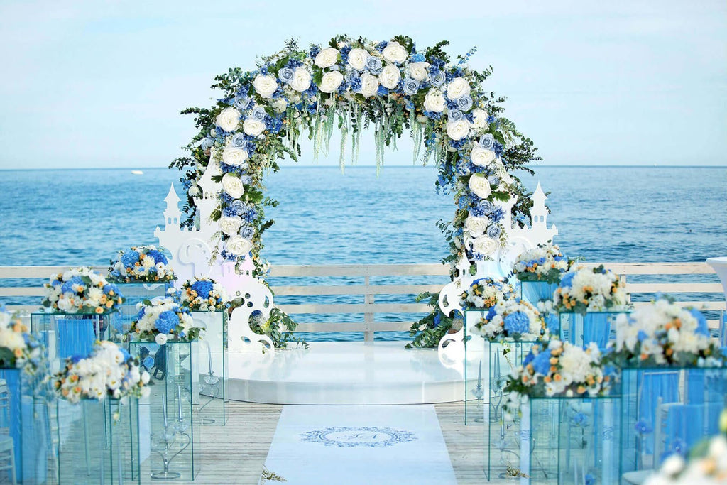 Wedding arch decorated with blue and white flowers, overlooking the ocean. A white aisle runner with a monogram is in the foreground.