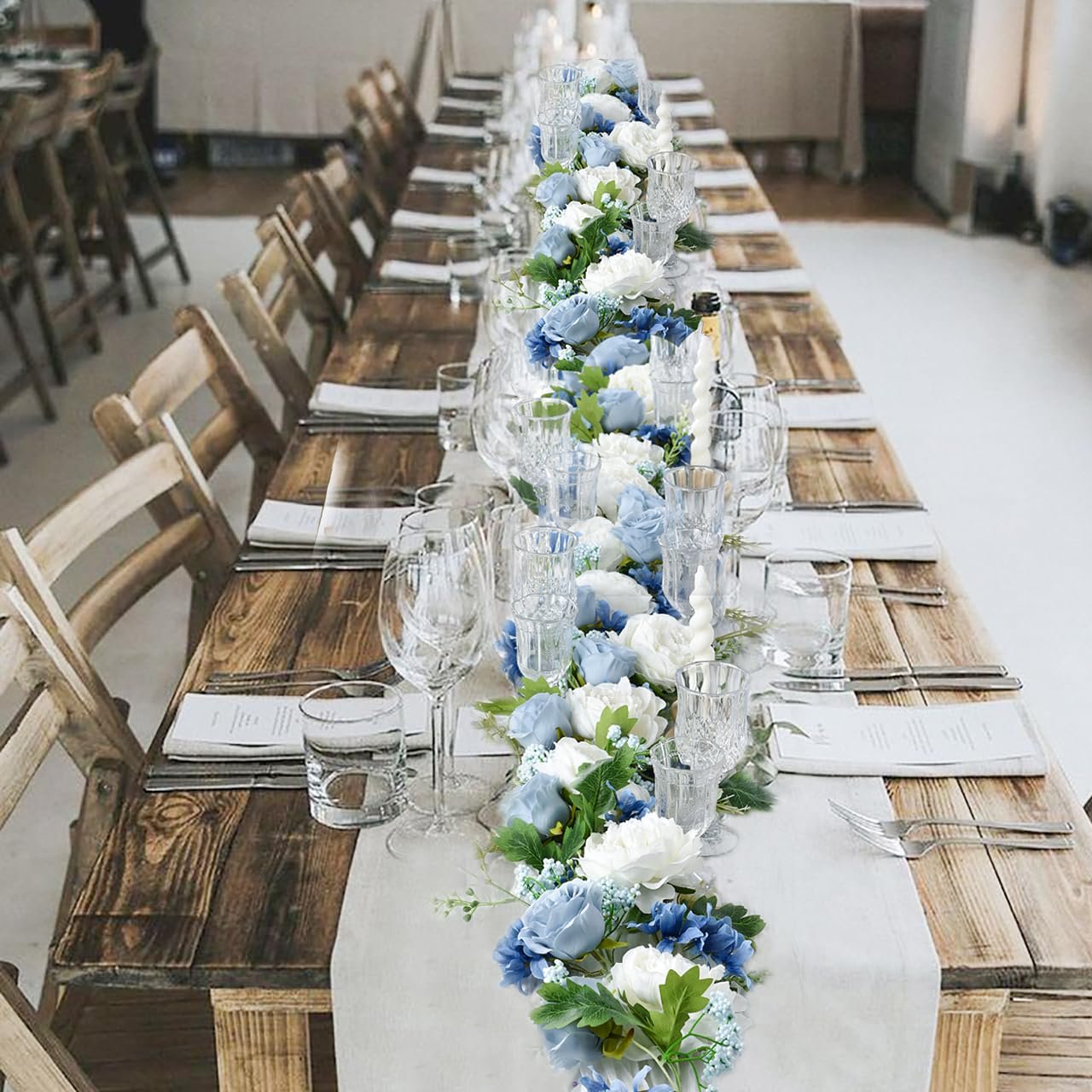 Blue and white artificial peony garland draped along a rustic wooden table set for a wedding reception.