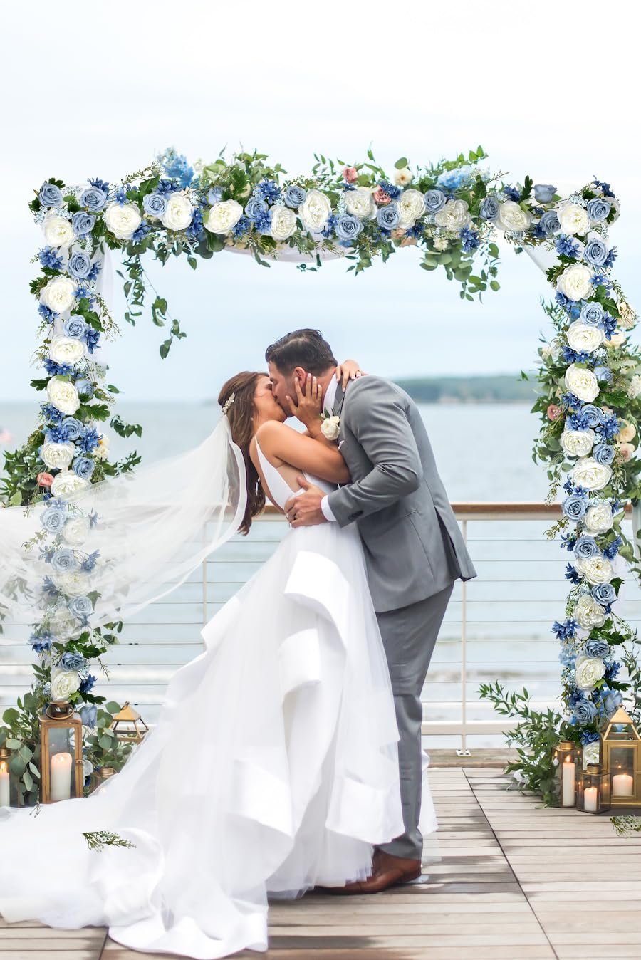 Bride and groom kissing under a wedding arch decorated with blue and white flowers and greenery.