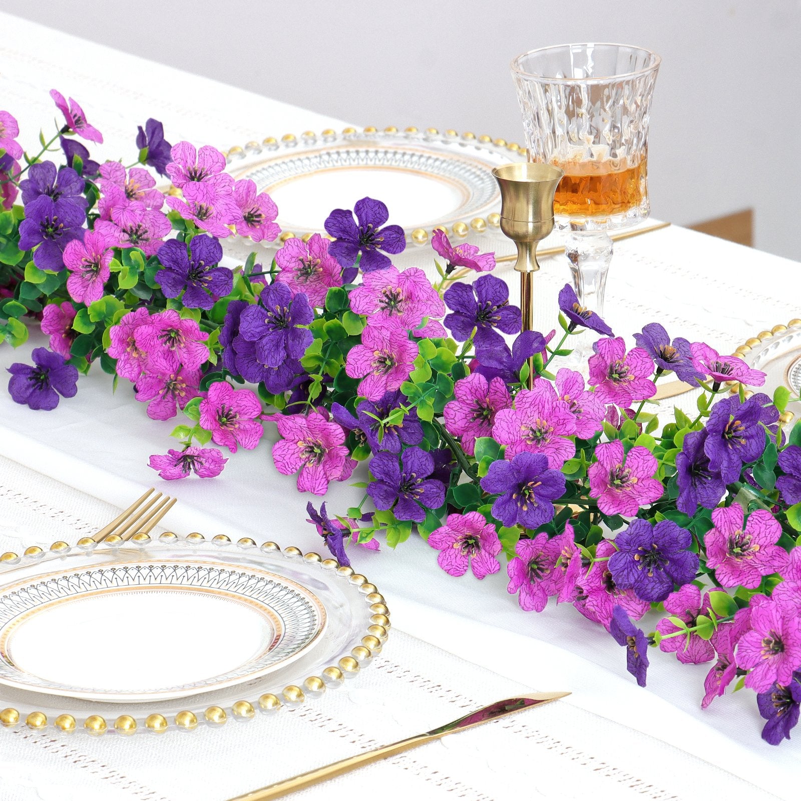 Artificial purple and pink daisy flower garland draped across a table setting with plates and a glass