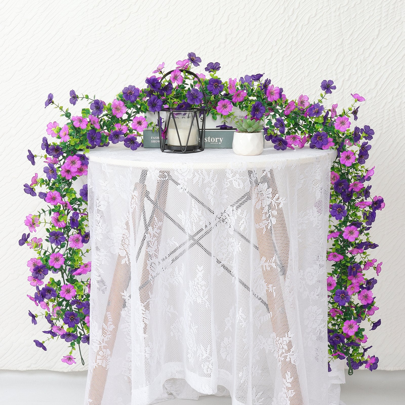 Artificial daisy flower garland with purple and pink blooms draped over a white lace-covered table.