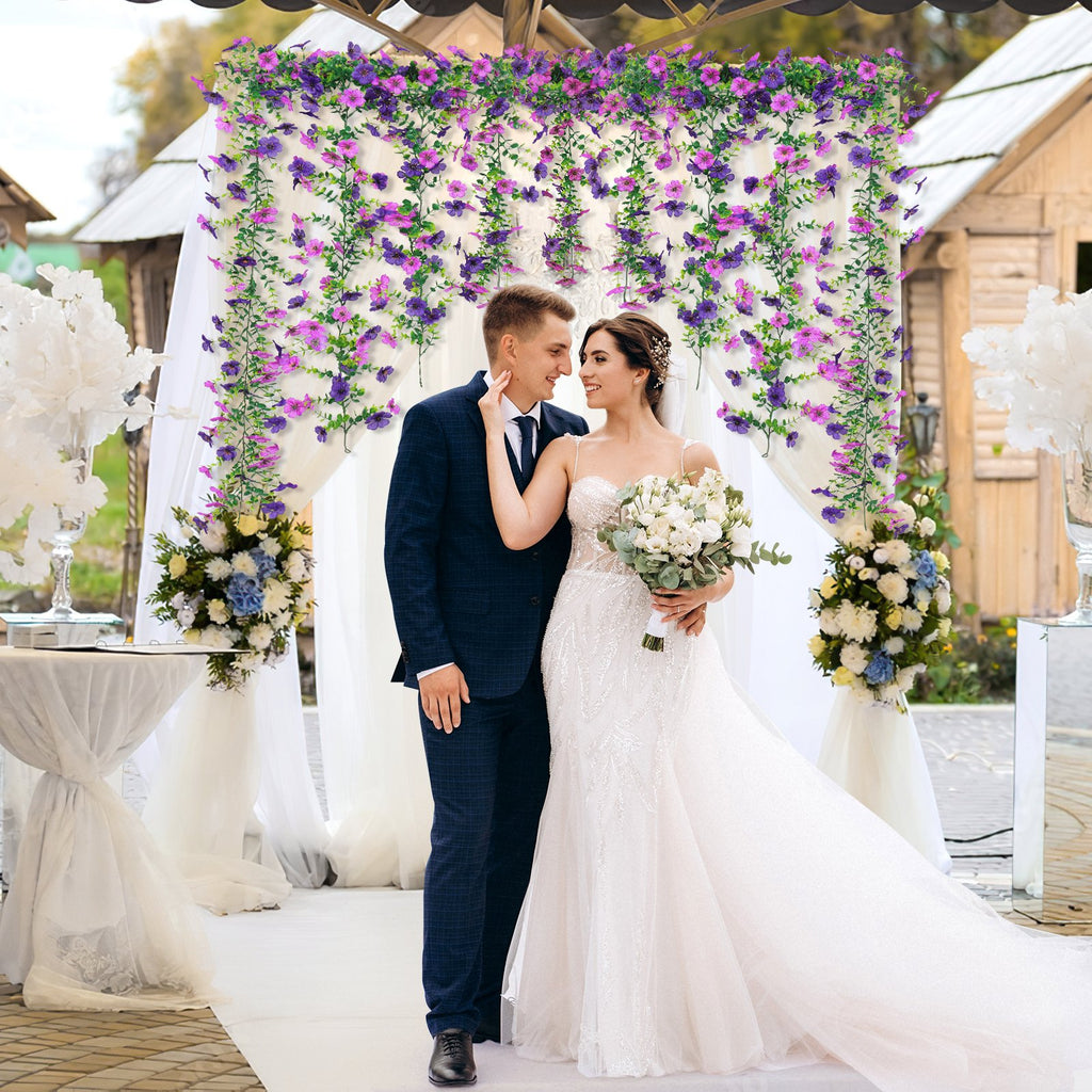 Wedding couple posing under a floral arch decorated with artificial purple and pink flowers.