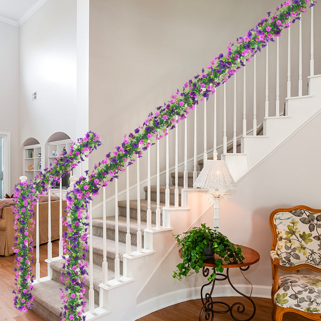 Two artificial daisy flower garlands with purple and pink flowers draped along a white staircase railing.