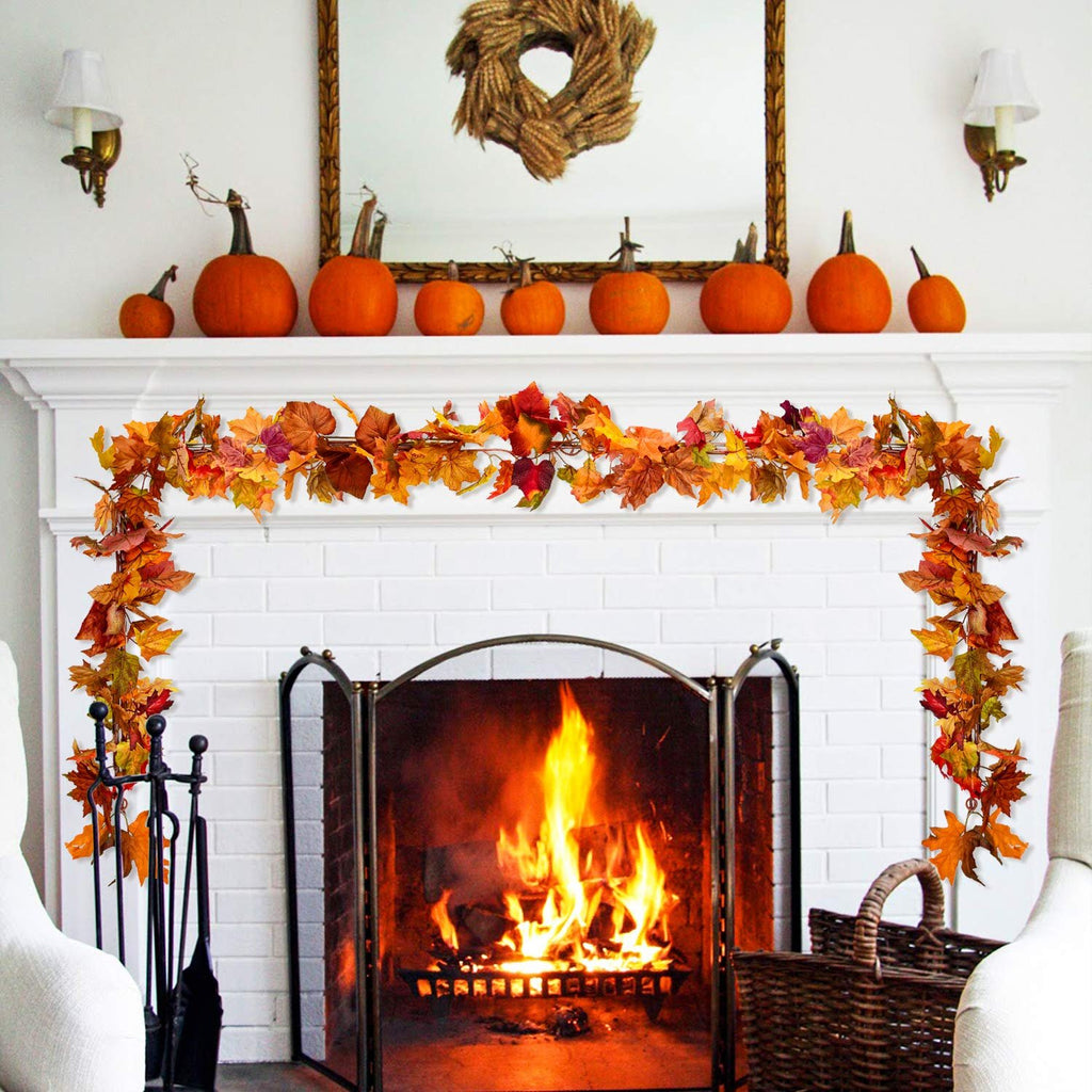 Artificial fall maple leaf garland draped over a fireplace mantel with pumpkins and a lit fireplace.