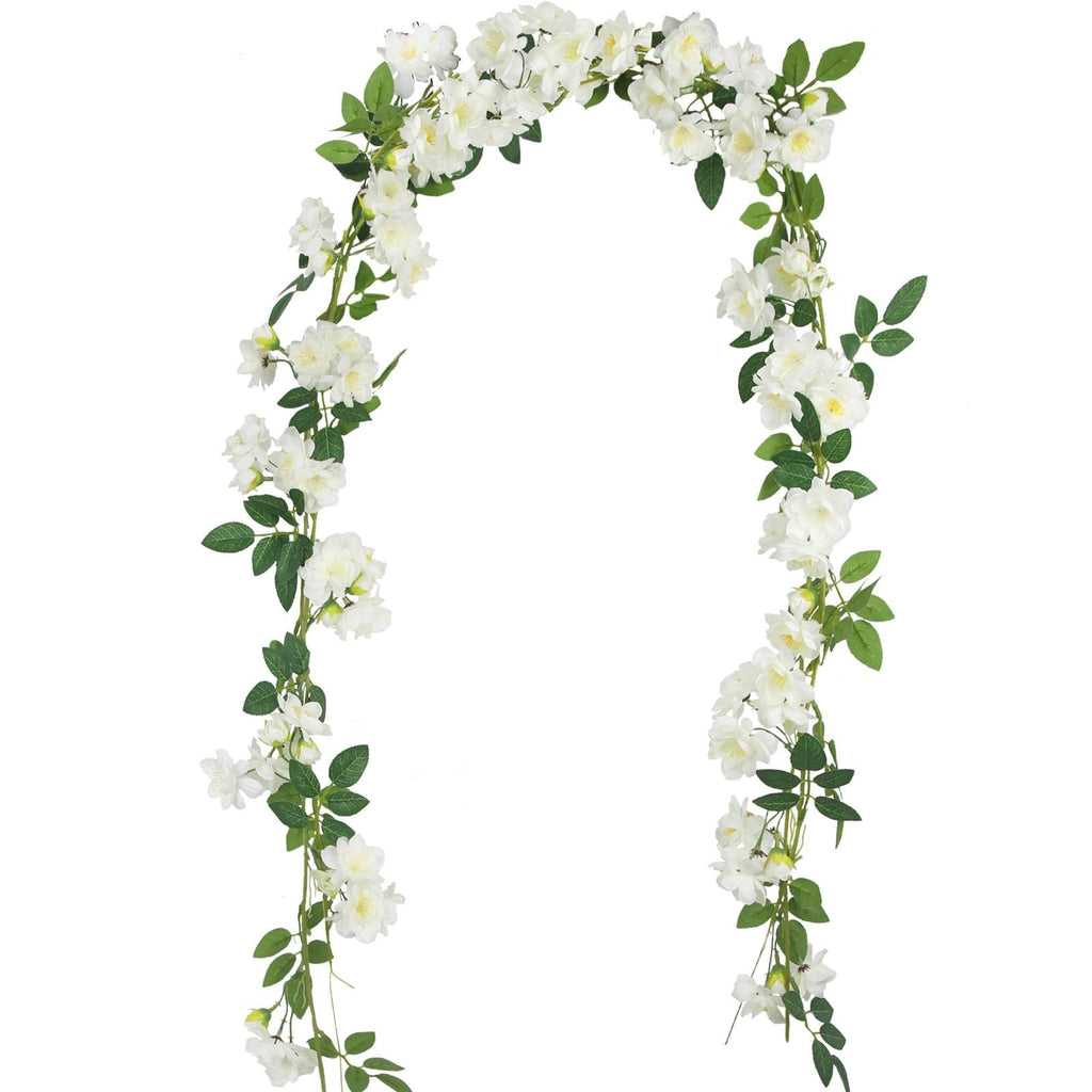 Artificial gardenia garland with white silk flowers and green leaves on a white background, shown draped in an arch shape.