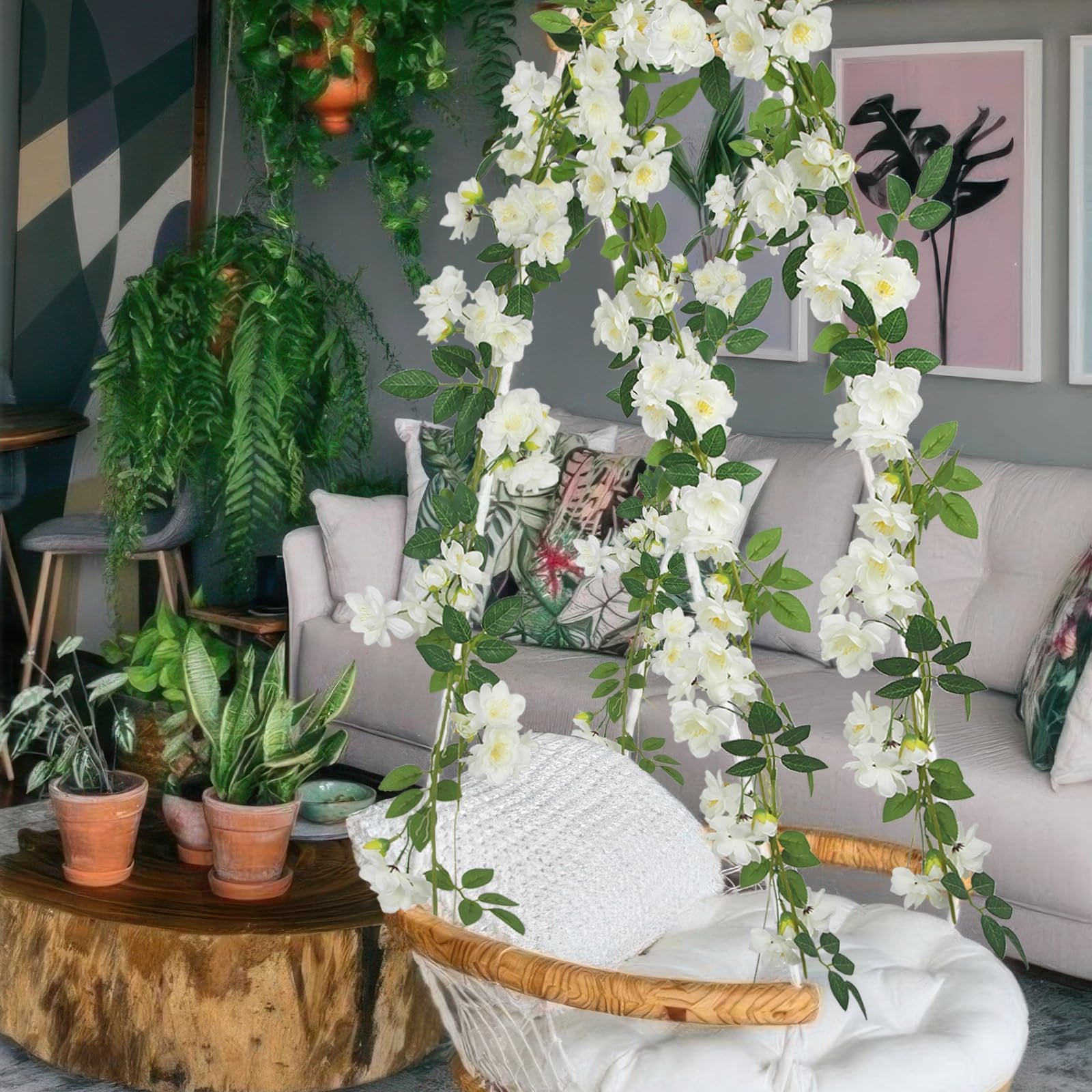 Two artificial gardenia garlands with white flowers and green leaves draped over a chair and sofa in a living room.