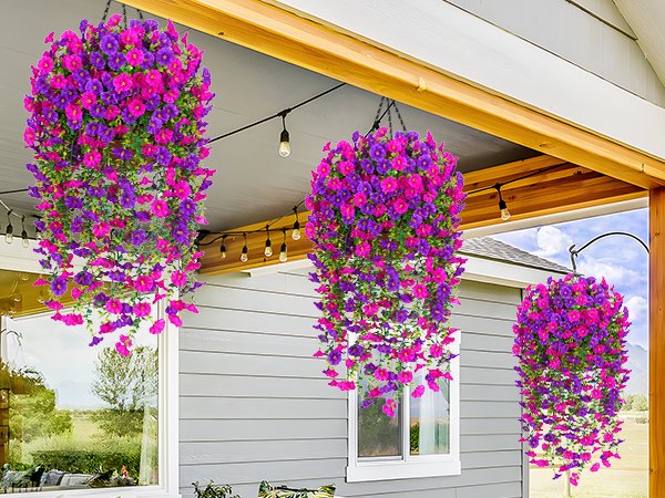 Three hanging baskets filled with artificial fuchsia and rose red petunia flowers, displayed on an outdoor porch.