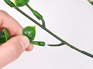 Hand attaching a green artificial flower stem to a larger branch against a white background