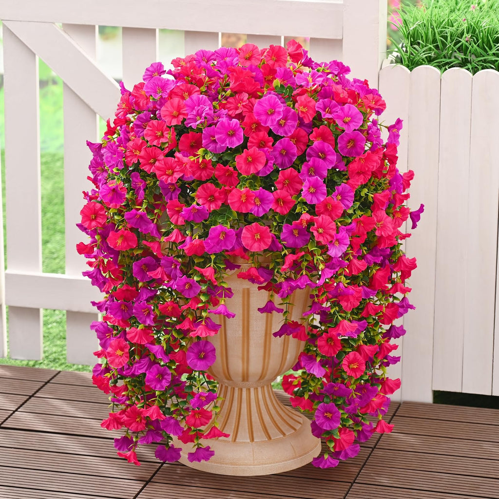 Two hanging artificial petunia flower arrangements in fuchsia and rose red colors, cascading from a decorative urn on a wooden deck.