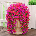 Two hanging artificial petunia flower arrangements in fuchsia and rose red colors, cascading from a decorative urn on a wooden deck.
