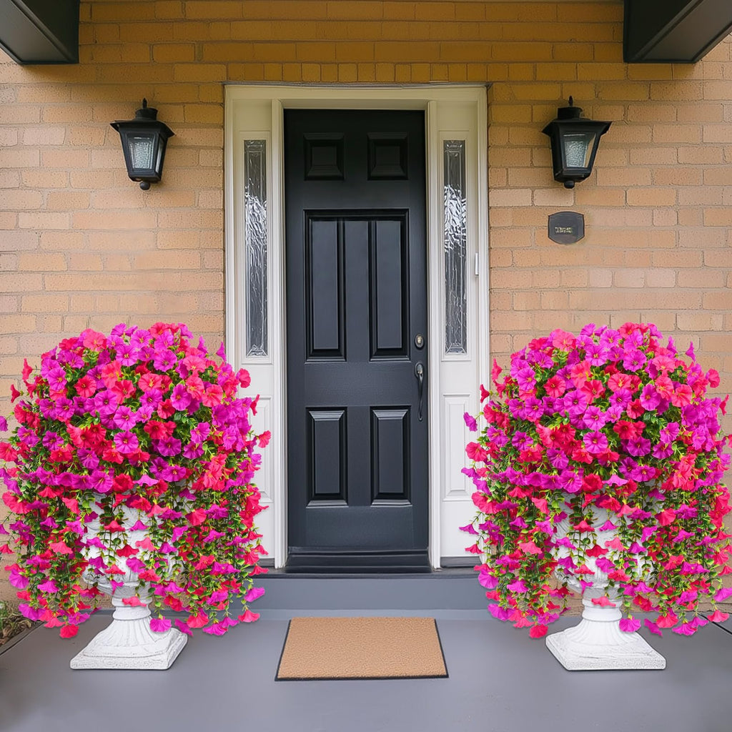 Two large planters filled with vibrant pink and fuchsia artificial petunia flowers flanking a dark front door.