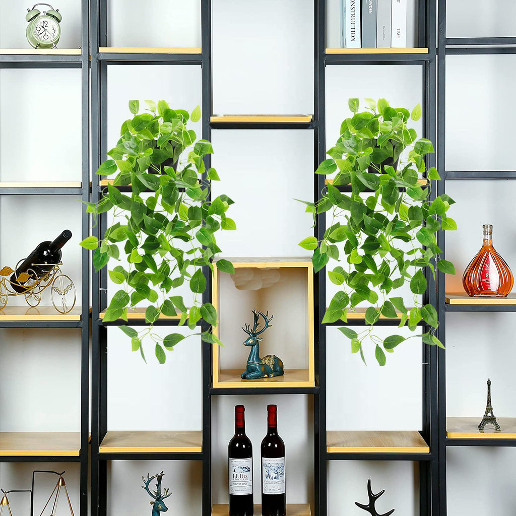 Two artificial hanging plants with green ivy vines in black pots displayed on a shelf.