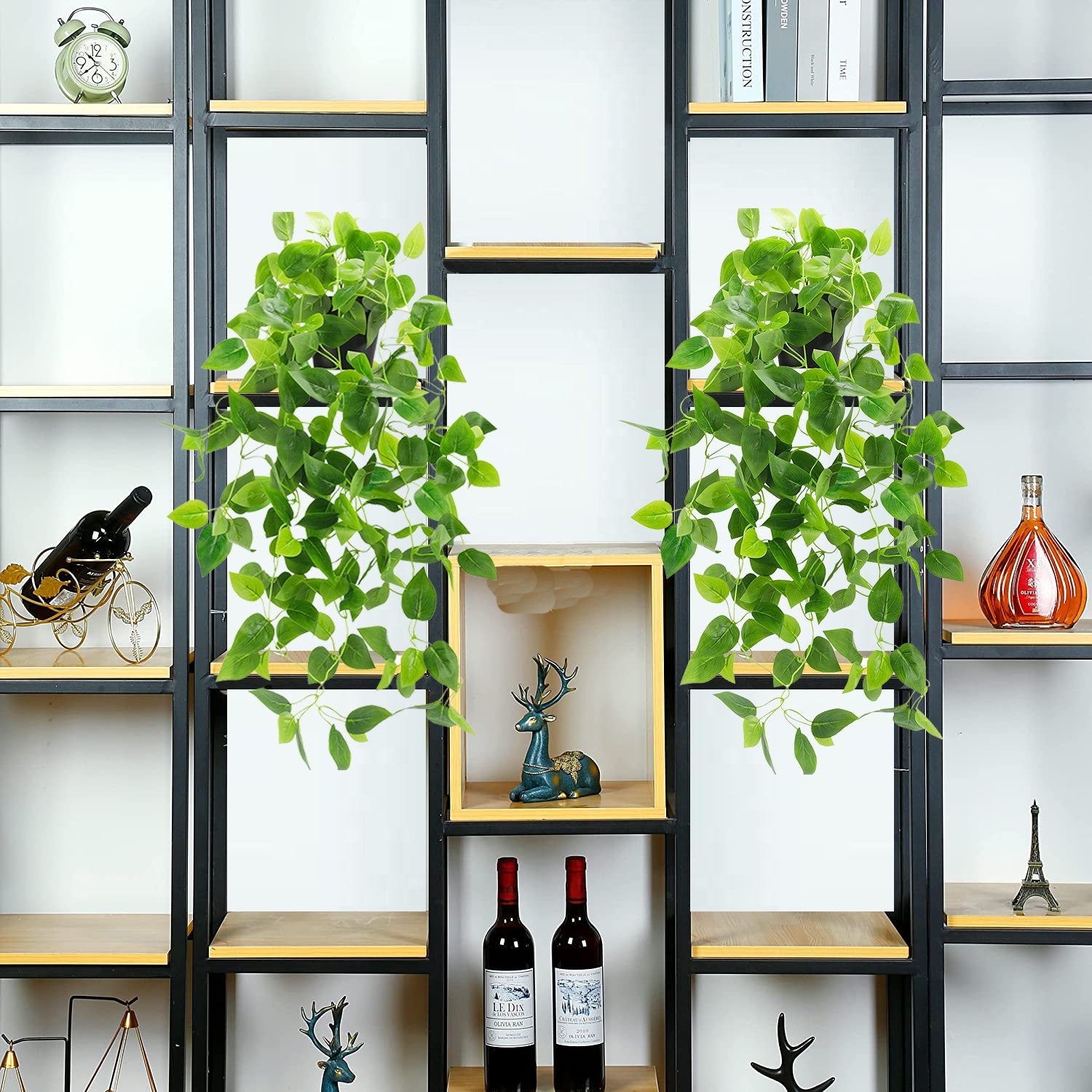 Two artificial hanging plants with green ivy vines in black pots displayed on a shelf.