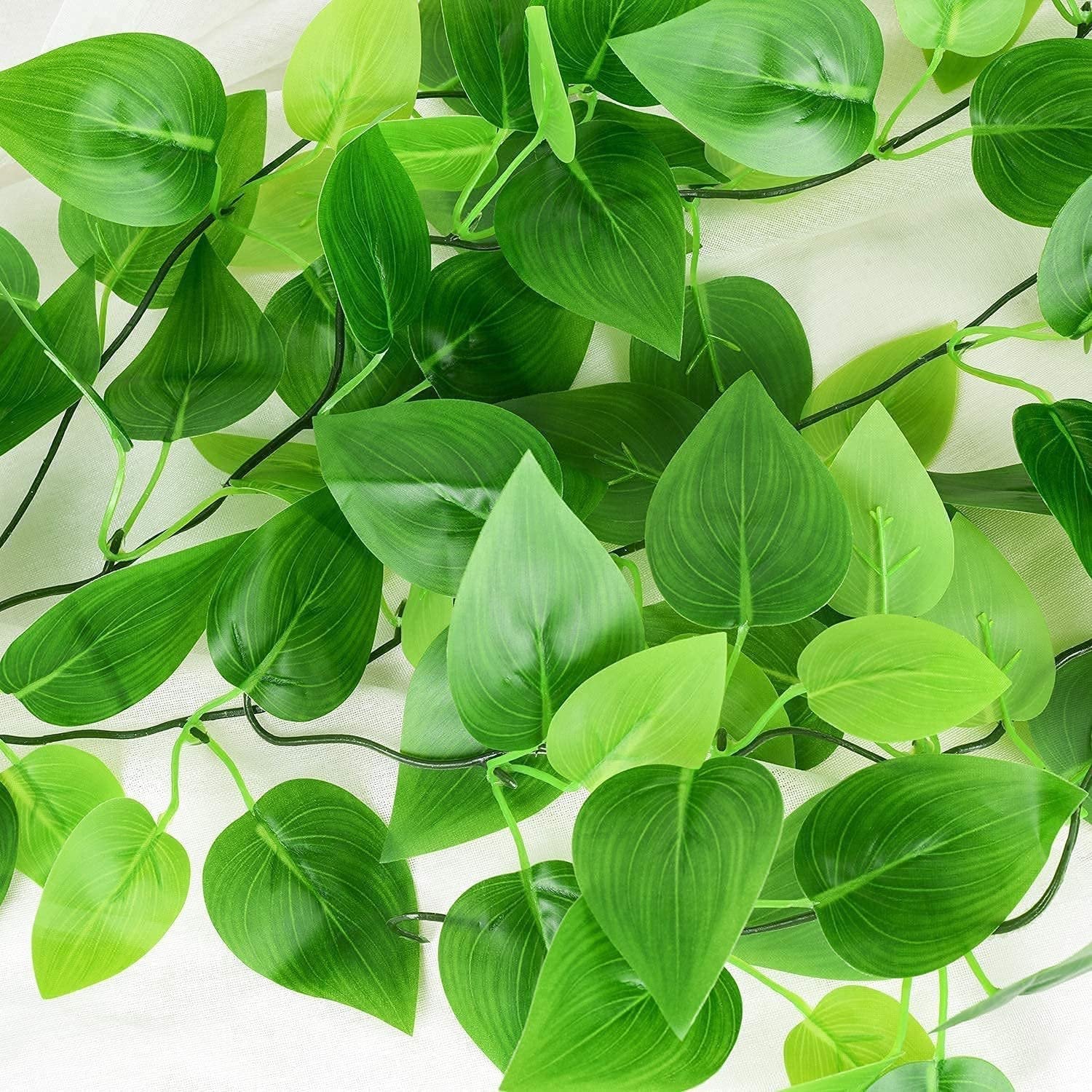 Close-up of lush green artificial ivy vines with detailed leaf veins, draped over a white textured surface.