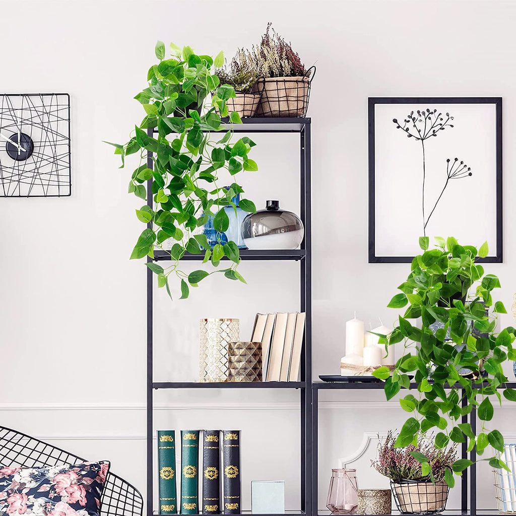 Two artificial hanging plants with green ivy vines in black pots on a shelf with decor