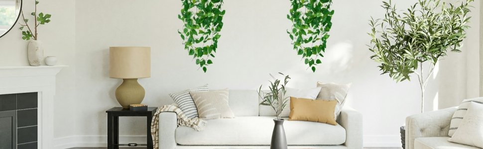 Two artificial ivy hanging vines with green leaves displayed in a living room setting above a sofa.