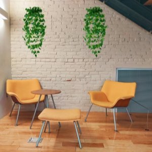 Two artificial ivy hanging vine arrangements with green leaves displayed on a white brick wall above yellow chairs and a small table.