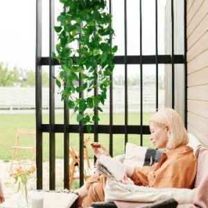 Woman reading on a couch under artificial ivy hanging vines on a patio