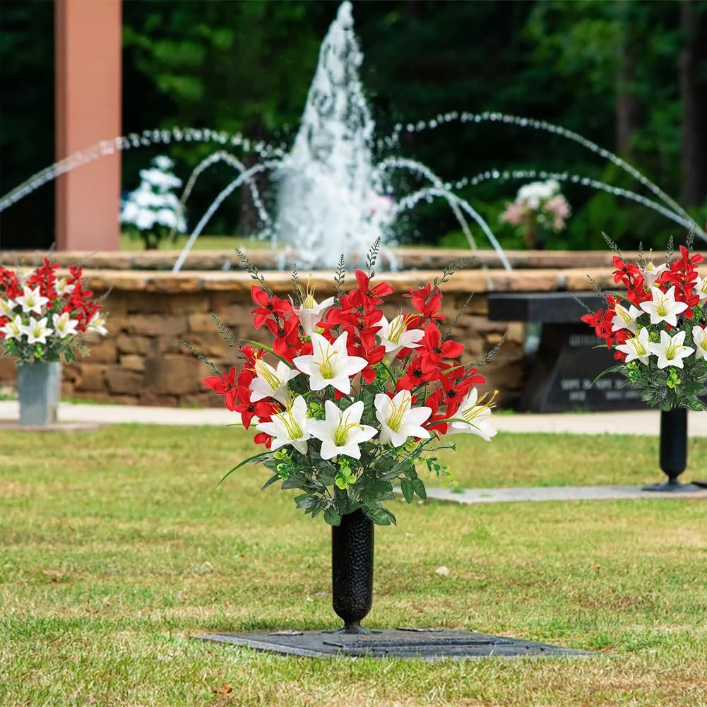 Two bouquets of artificial red and white lilies and gladiolus flowers in black vases, placed on a grassy area with a fountain in the background.