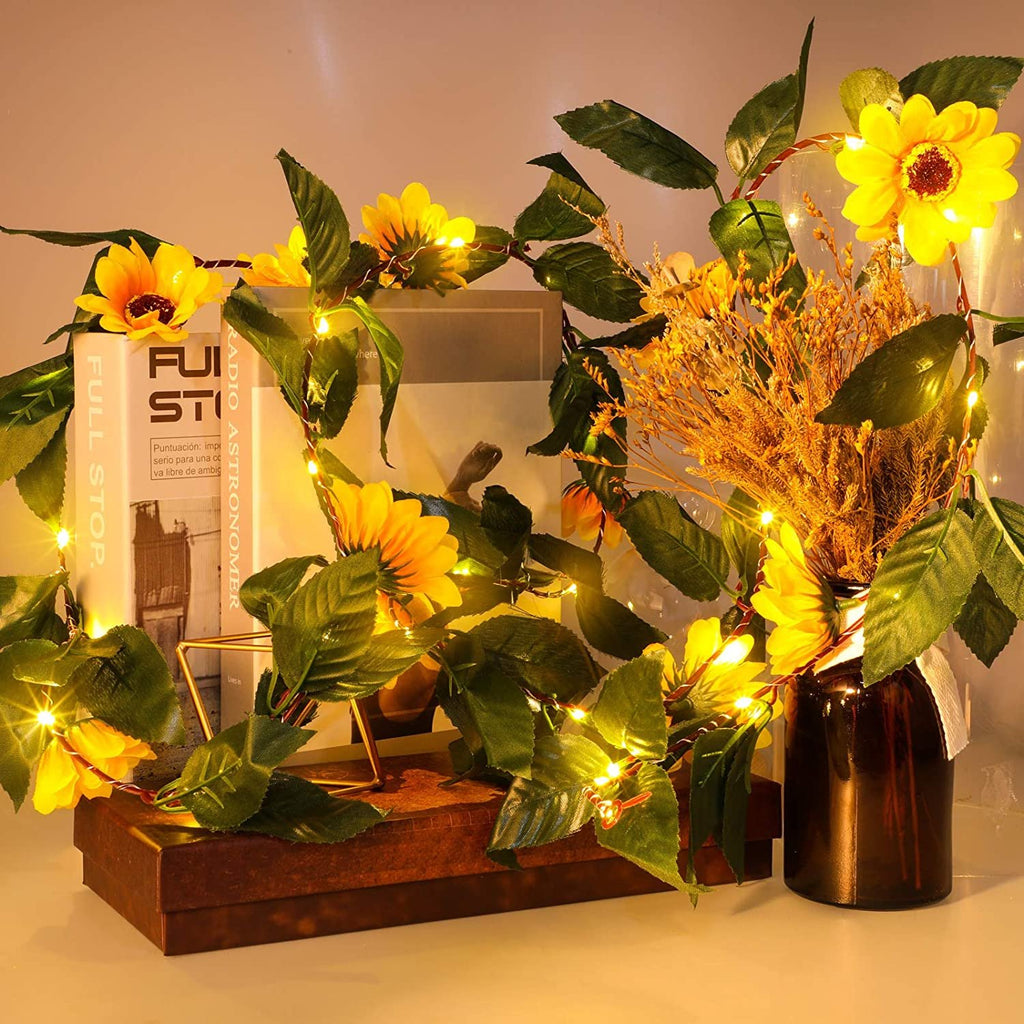 Artificial sunflower garland with LED string lights draped around books and a vase of dried flowers.