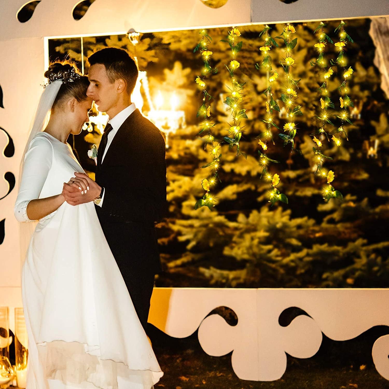 Newlyweds dancing with artificial sunflower garland lights draped behind them
