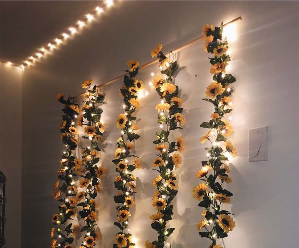 Four artificial sunflower garlands with LED string lights hanging vertically on a wall.