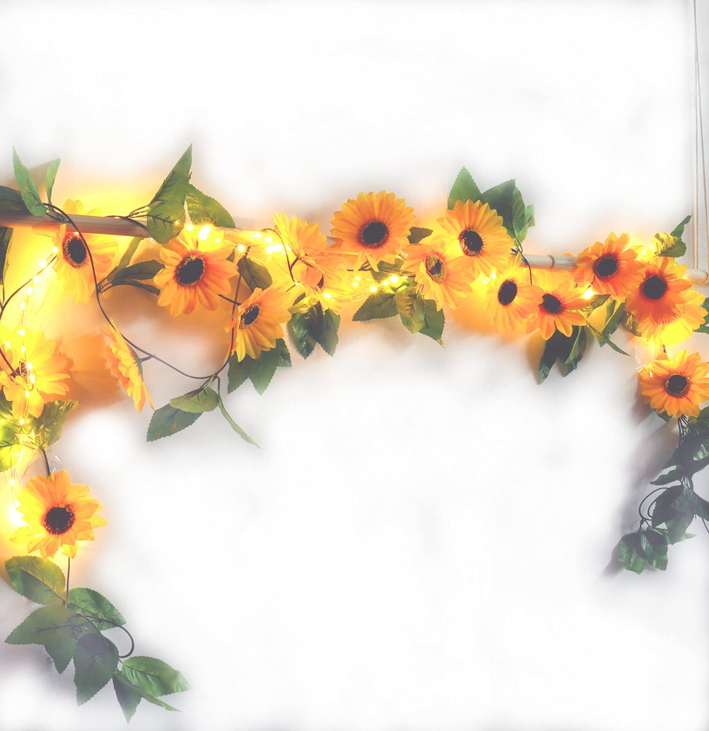 Artificial sunflower garland with LED string lights draped over a wooden rod against a white background.