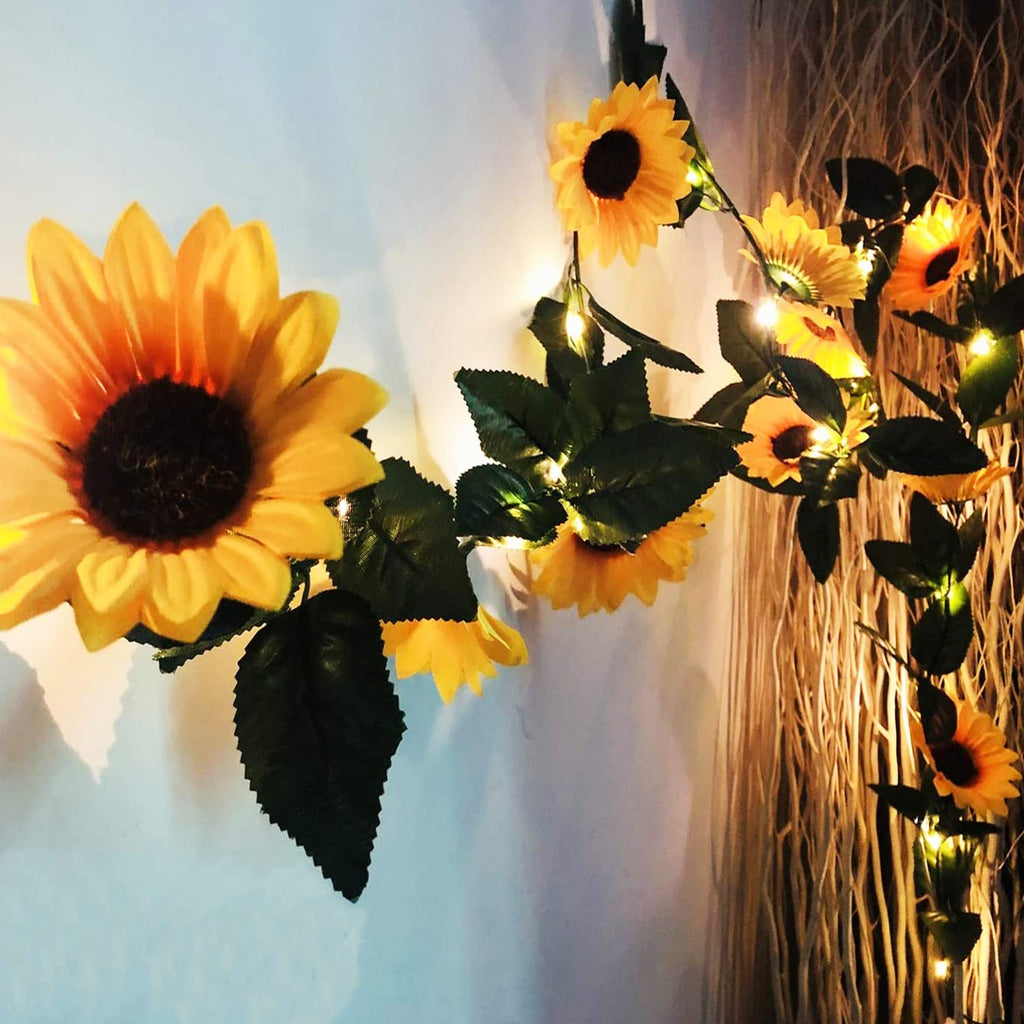 Artificial sunflower garland with LED string lights draped on a wall with decorative branches.