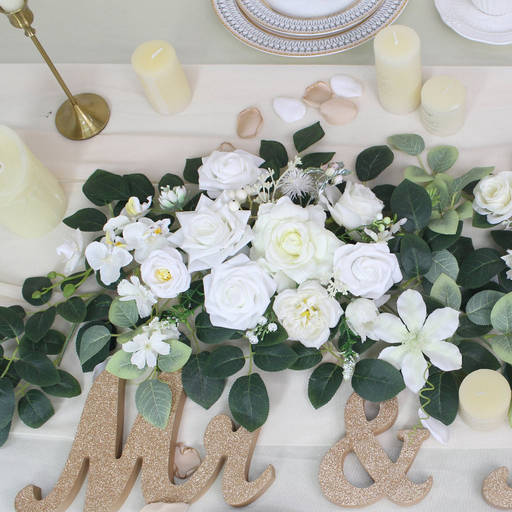 White artificial wedding arch flower garland with greenery and gold 'Mr & Mrs' letters on a table setting