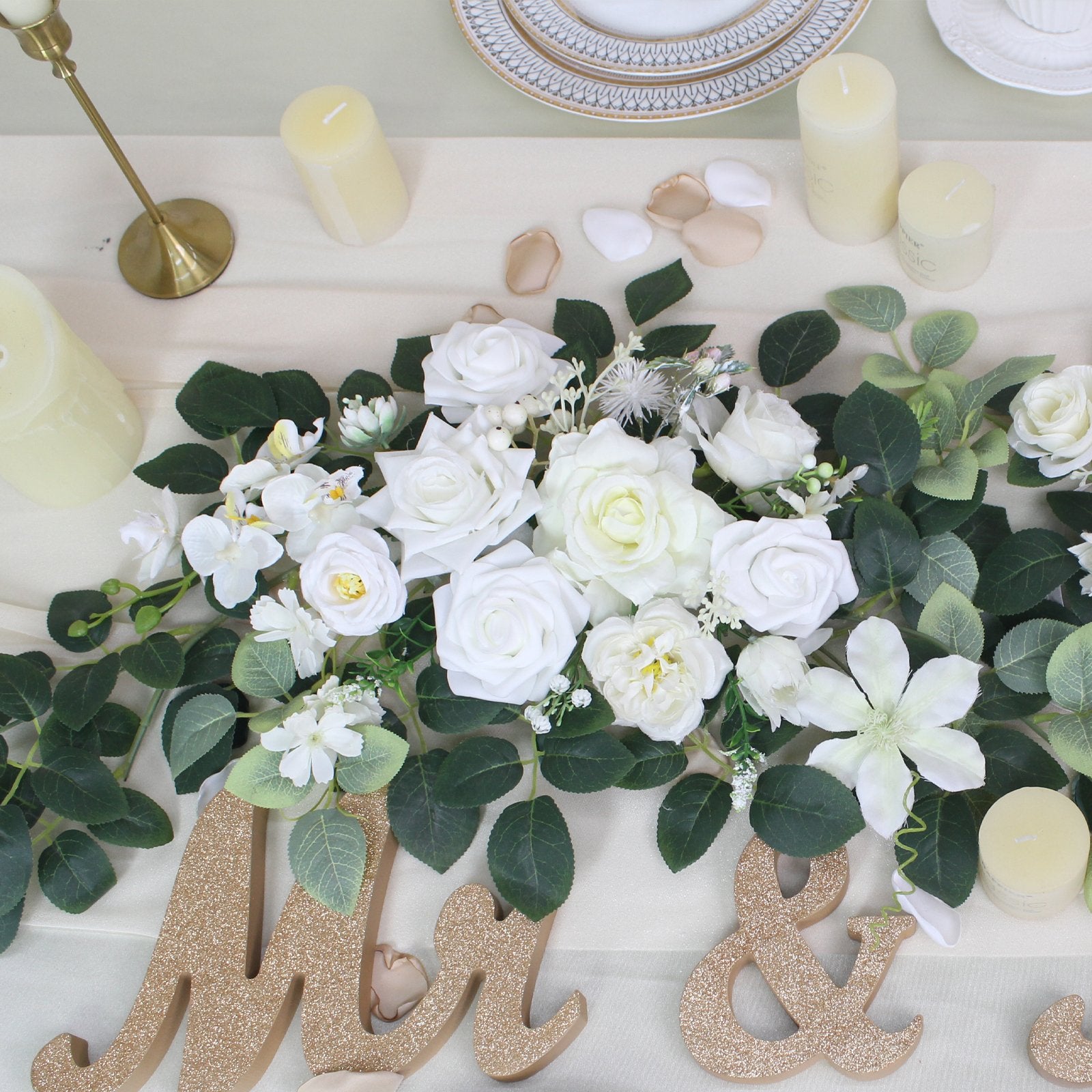 White artificial wedding arch flower garland with greenery and gold 'Mr & Mrs' letters on a table setting