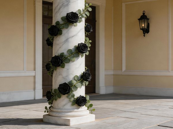 Black artificial rose garland with green leaves wrapped around a marble column outdoors.