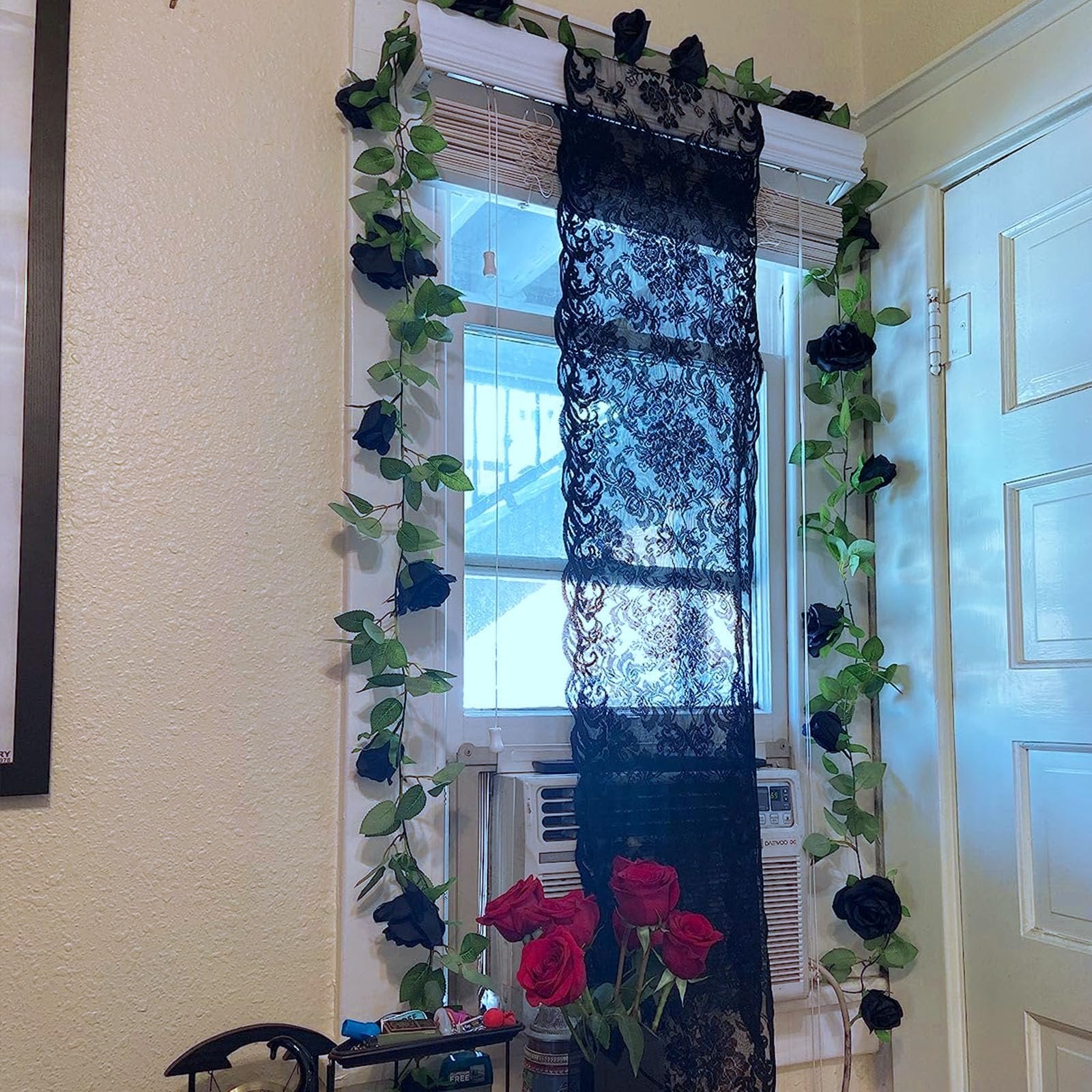 Black artificial rose garland draped around a window frame with a black lace curtain.