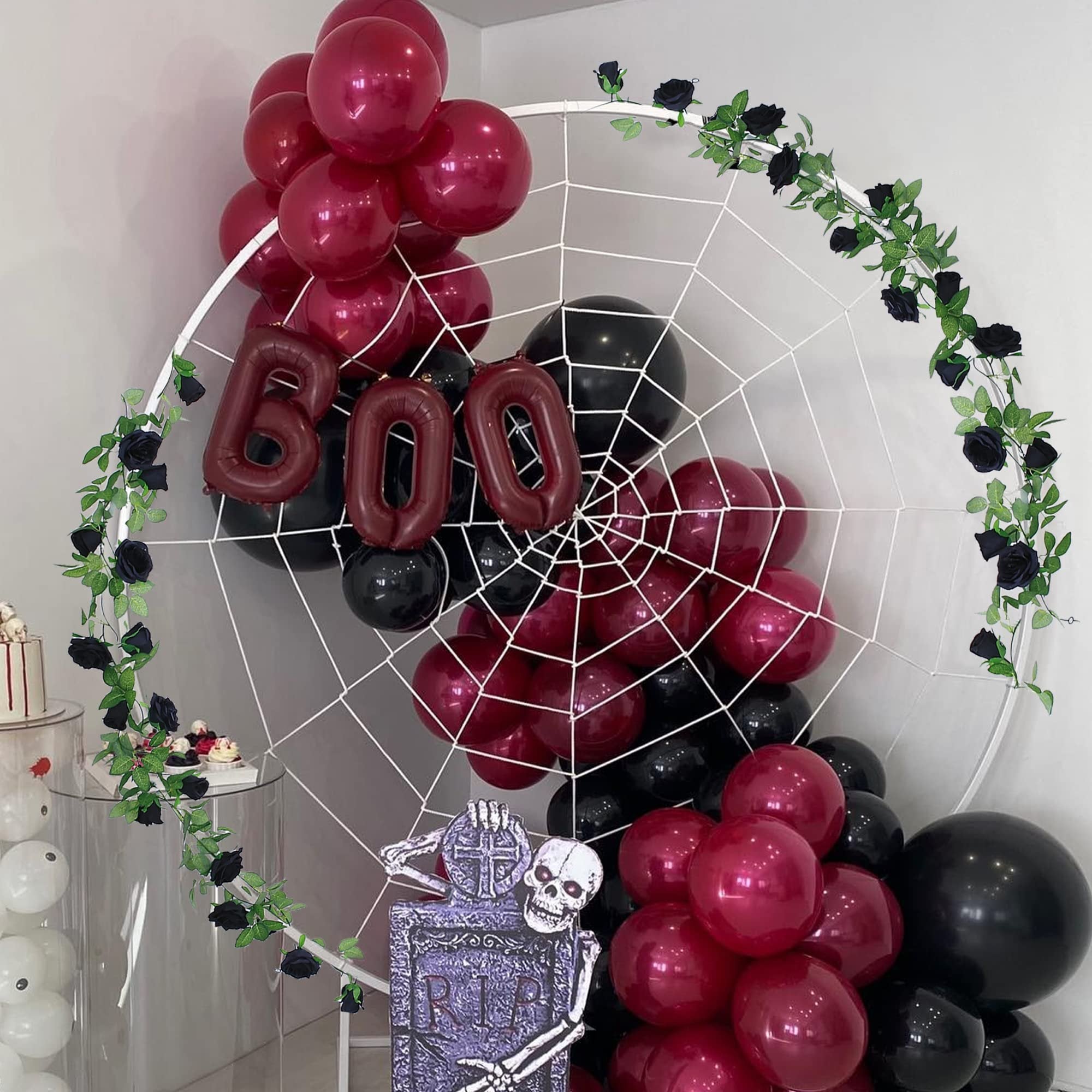 Halloween balloon arch with black and maroon balloons, a spiderweb backdrop, and black rose garlands.