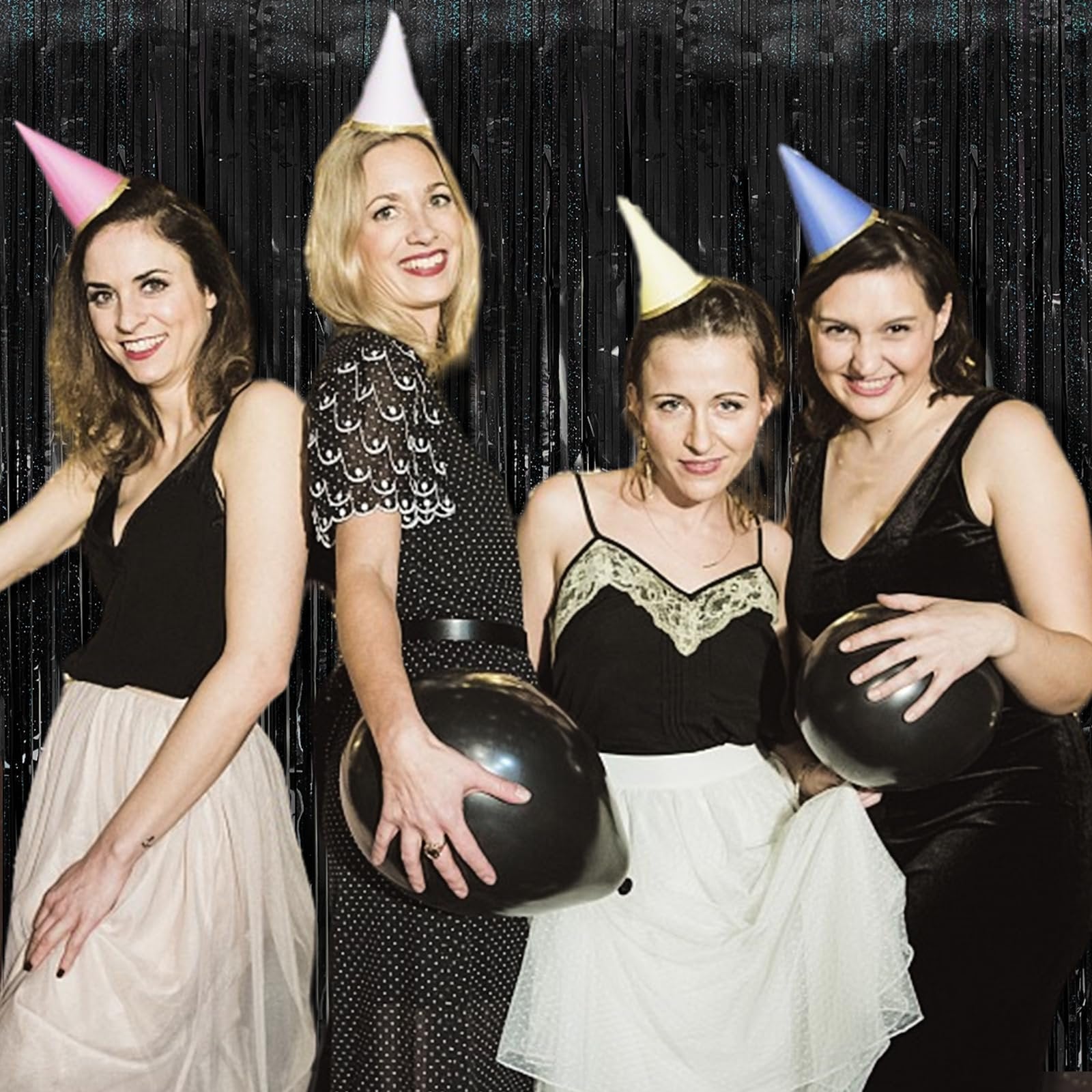 Four women in party hats holding balloons in front of a black tinsel backdrop