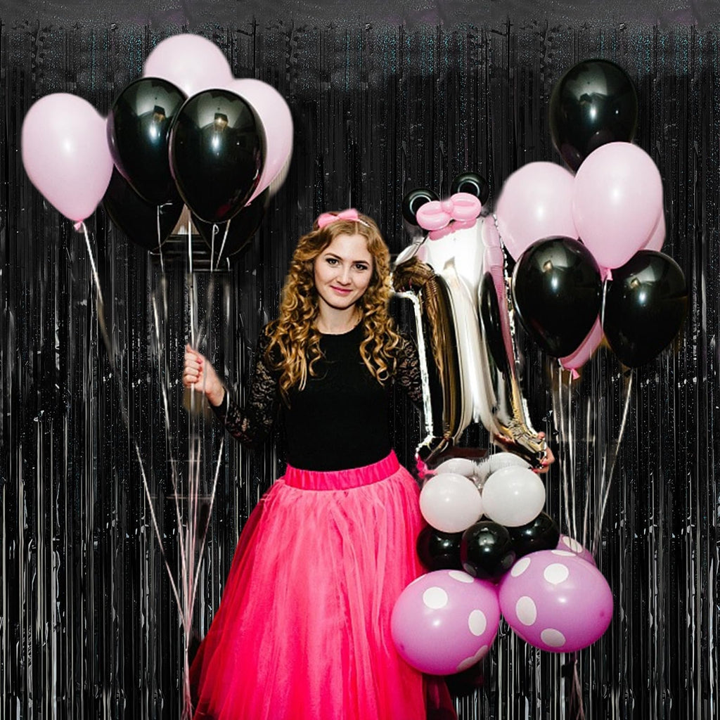 Woman holding balloons and a foil number 1 balloon in front of a black tinsel curtain backdrop