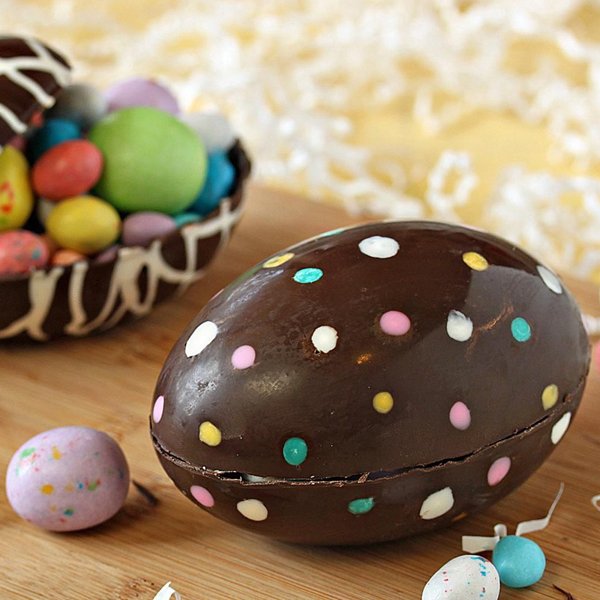 Chocolate Easter egg with colorful polka dots, next to a basket of candy eggs and smaller speckled eggs.
