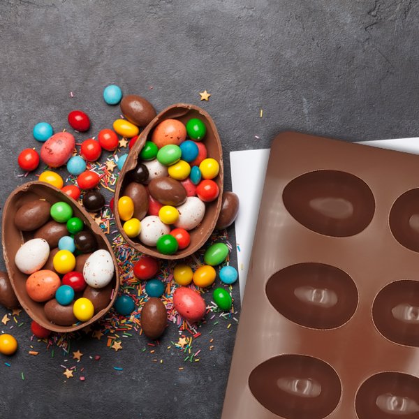 Easter egg chocolate molds filled with colorful candies and sprinkles, with a silicone mold on the side