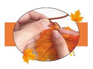 Hands assembling an artificial maple leaf garland with orange and yellow leaves