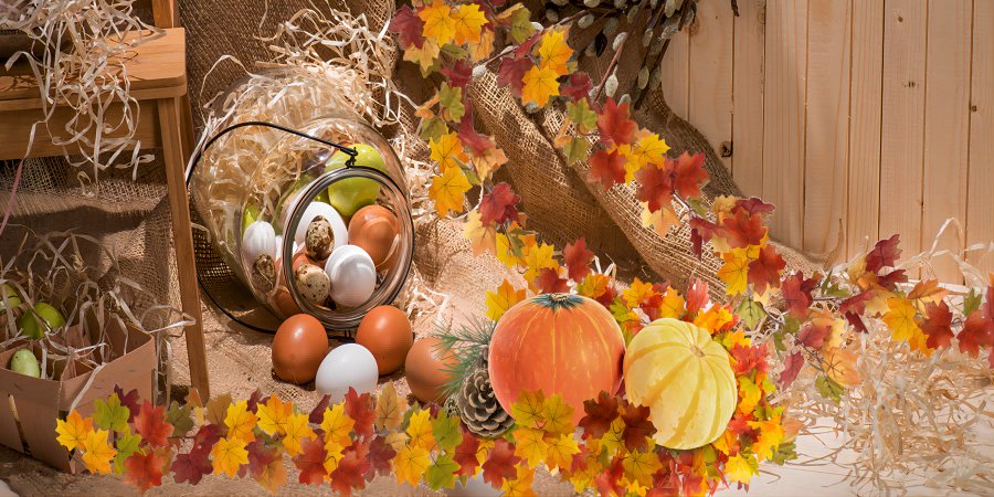 Autumn harvest display with pumpkins, eggs in a glass jar, and fall leaves garland on burlap and wood background