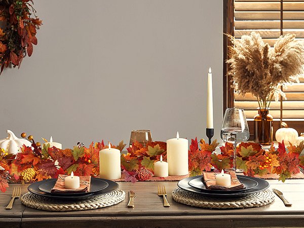 Autumn table setting with maple leaf garland, candles, plates, and pumpkins
