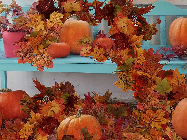 Autumn maple leaf garland and pumpkins arranged on a blue bench and surrounding area.