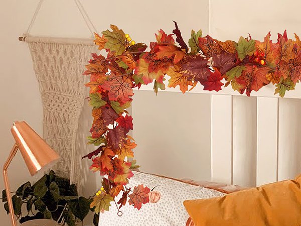 Autumn maple leaf garland with small lights draped over a white surface, next to a macrame wall hanging and a copper lamp.