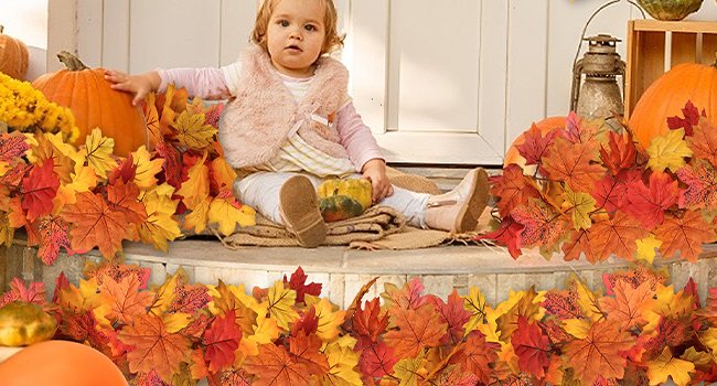 Toddler sitting on porch steps surrounded by fall maple leaf garlands and pumpkins.