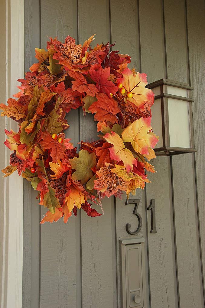 Autumn maple leaf wreath hanging on a gray paneled door next to a light fixture and house number 31.