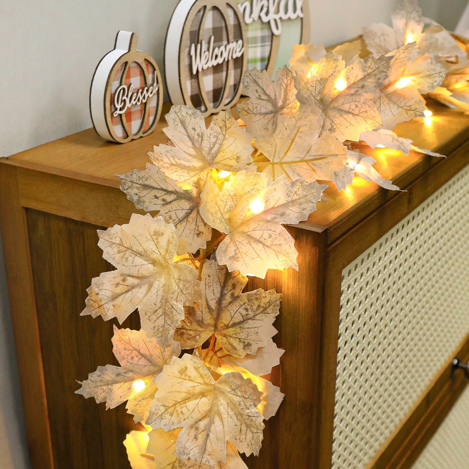 Fall maple leaf garland with warm LED lights draped over a wooden surface with decorative pumpkins.