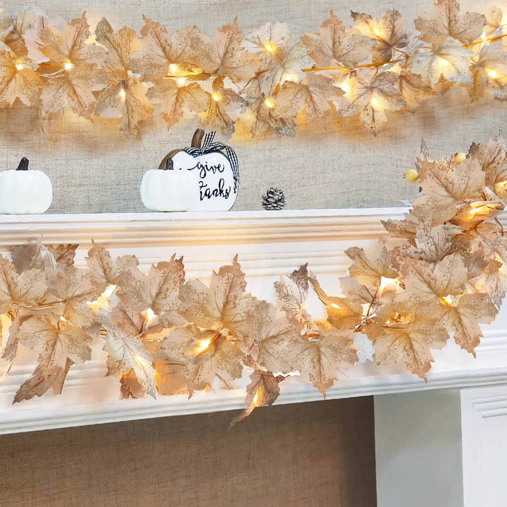 Two strings of artificial maple leaf garland with warm LED lights draped over a mantelpiece with decorative pumpkins.